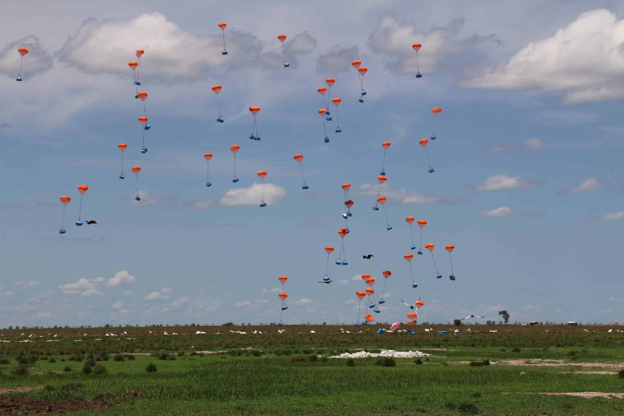 Dozens of orange Skylife canopies descending over a drop zone in South Sudan