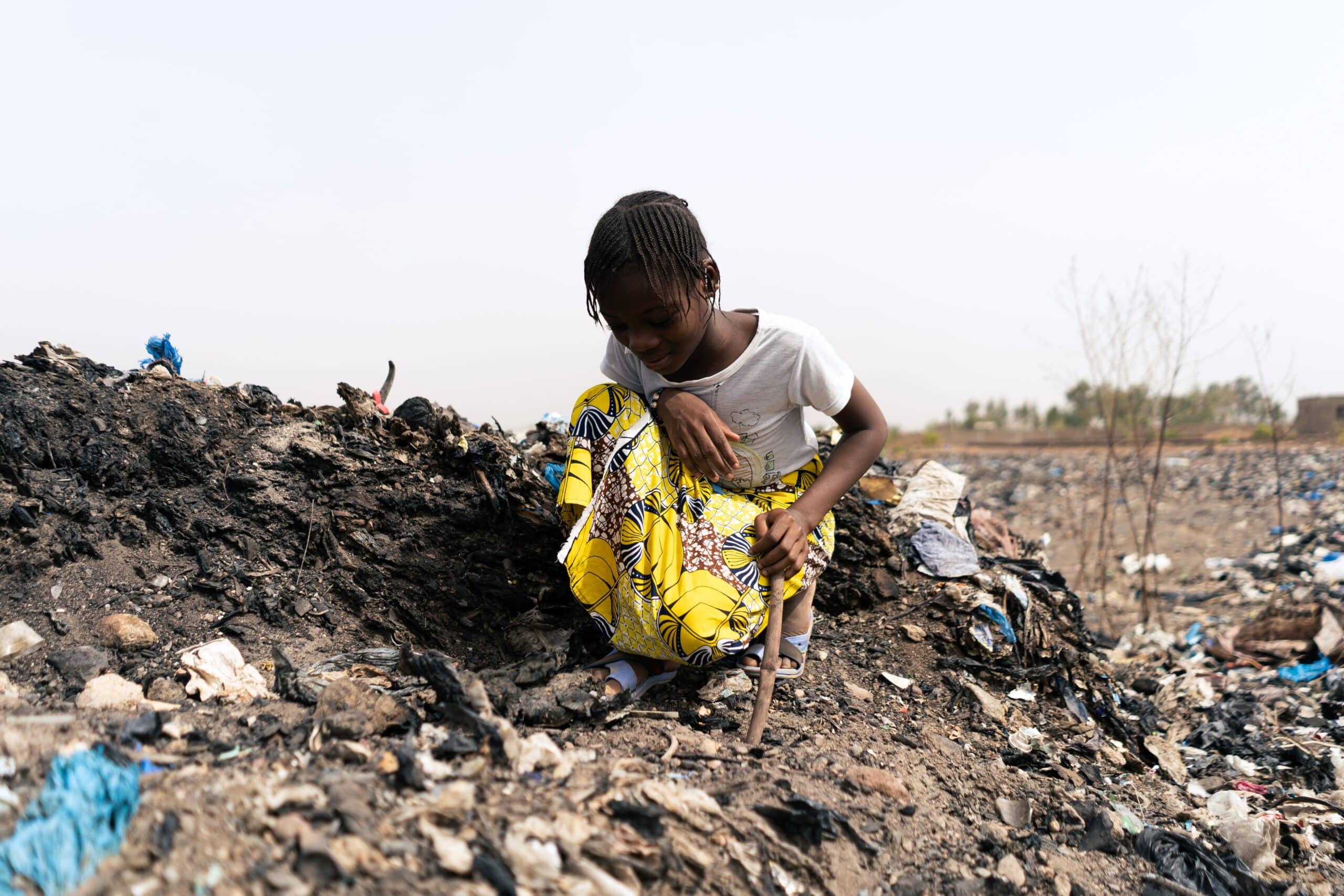 A young girl crouched in a disaster-affected landscape